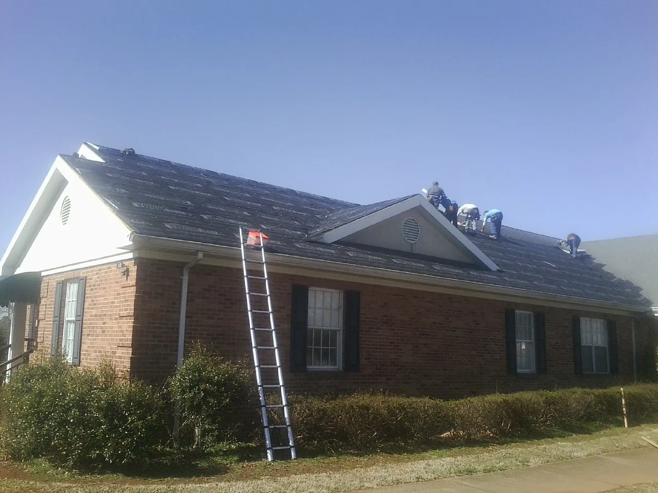 Crew tearing shingles off a brick ranch roof with a ladder set — Metal Roof Repair work by our crew in Alamo