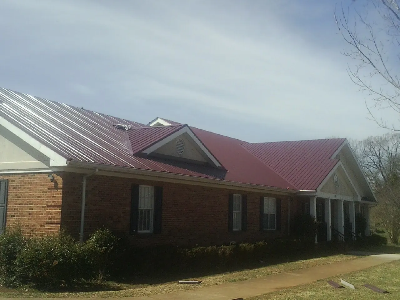 Red metal roof with gabled entries on a long brick building, from a Hail Damage Roof Repair job in Alamo