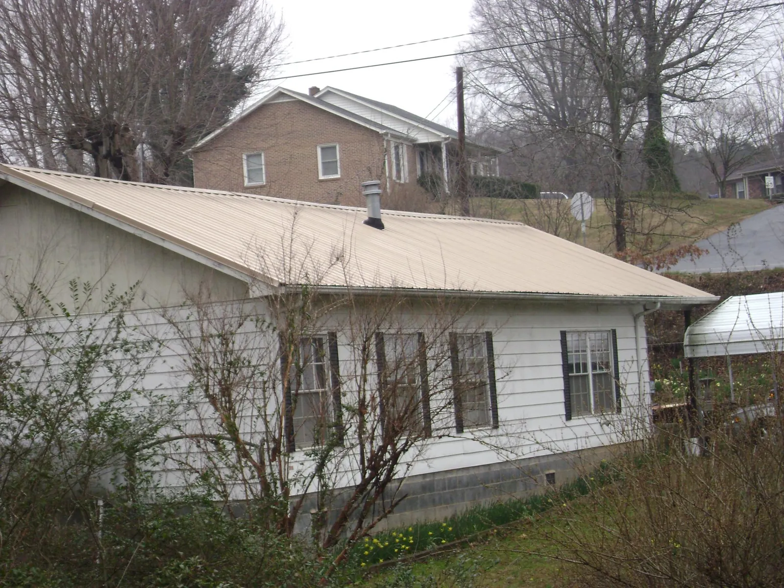 Tan metal roof on a white sided house set into a hillside — Commercial Roofing by Roofing Brothers in Alamo